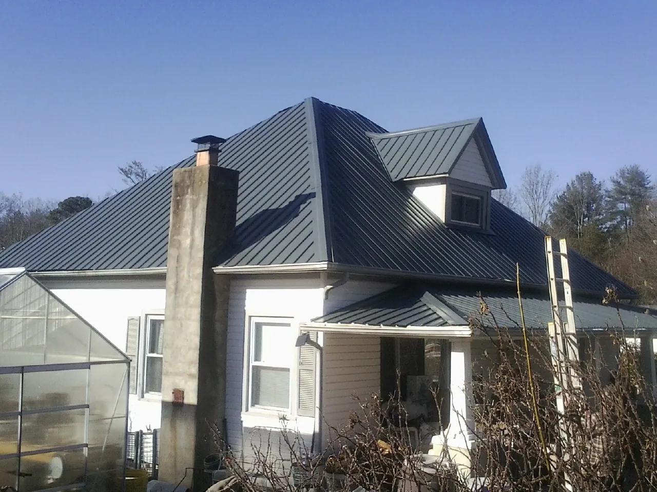 Dark blue standing seam metal roof on a white farmhouse with dormer — Slate & Tile Roof Repair by Roofing Brothers in Croton