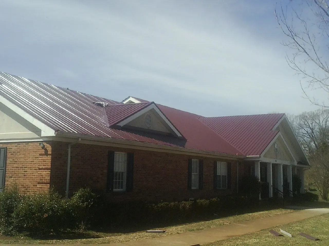 Red metal roof with gabled entries on a long brick building, from a Hail Damage Roof Repair job in Croton