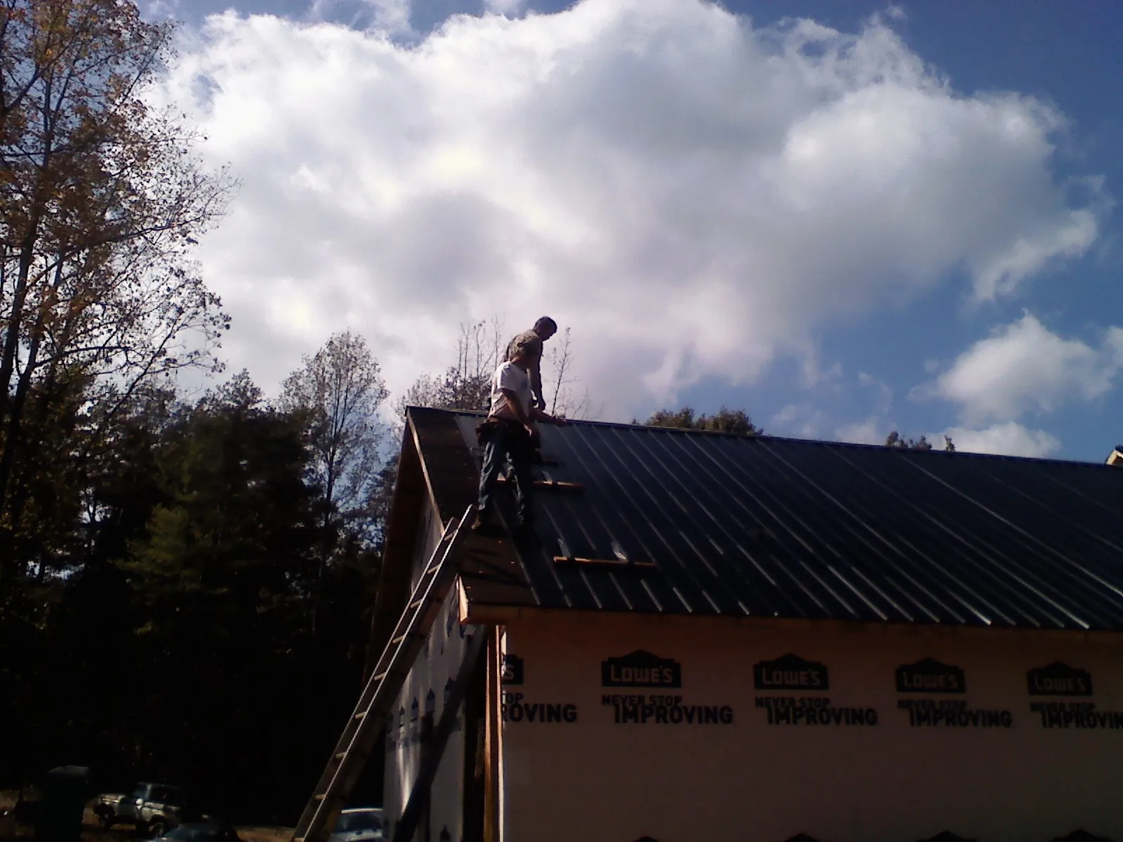Roofer fastening dark metal panels high against a cloudy sky, from a Roof Inspection job in Croton