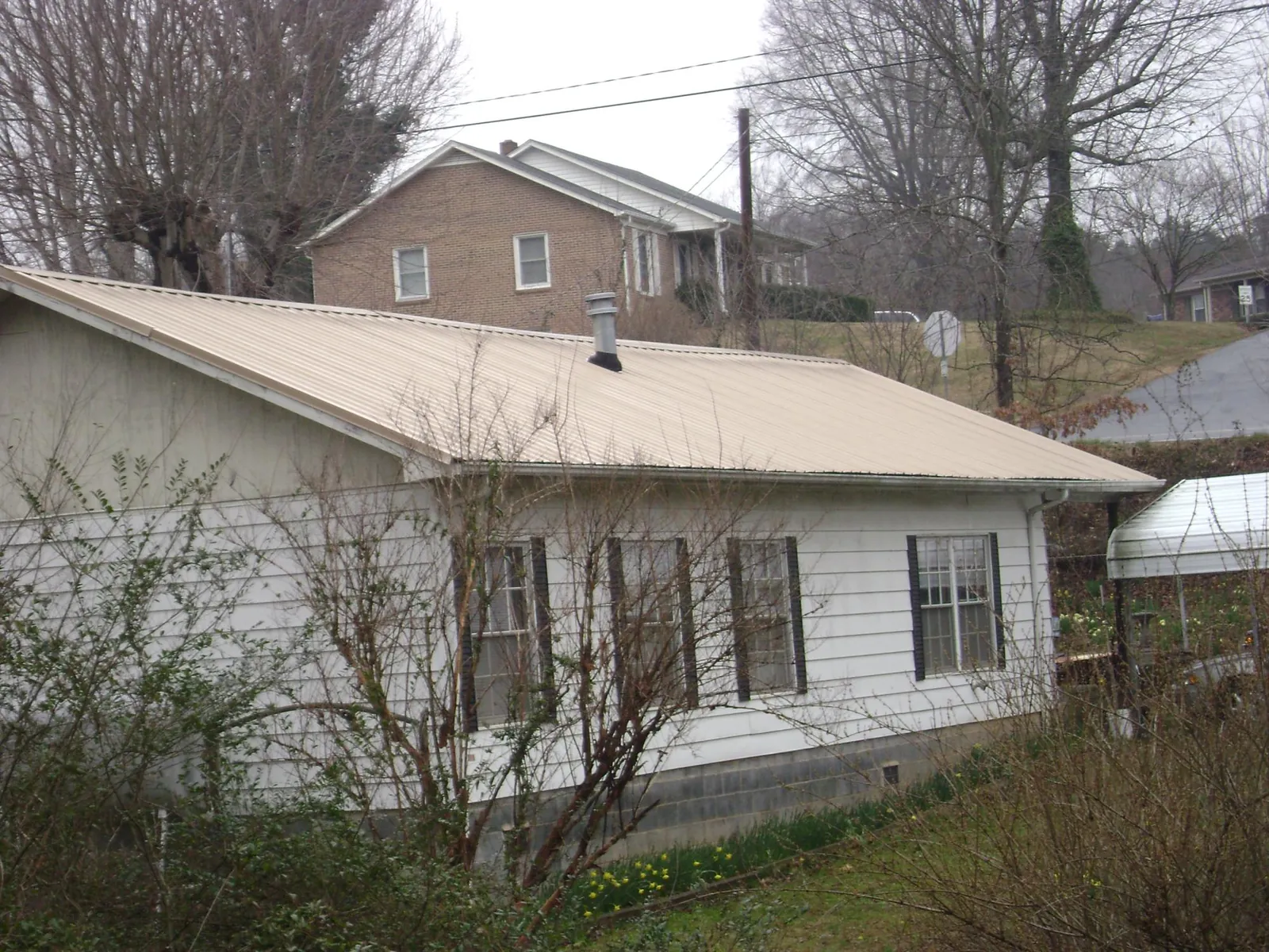 Tan metal roof on a white sided house set into a hillside — Commercial Roofing by Roofing Brothers in Croton